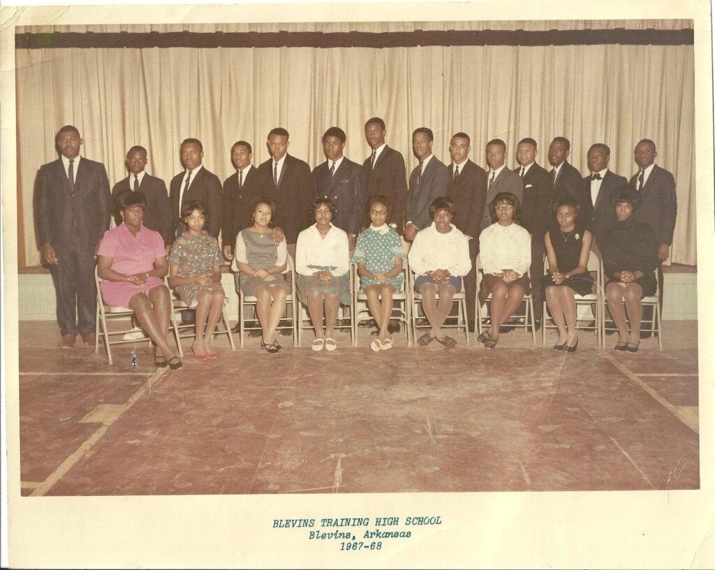 Formal portrait of the Blevins Training High School class of 1967–68: young men in suits stand behind a row of seated young women in front of a stage curtain.