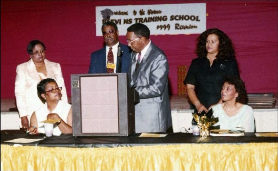 Alumni gathered at the head table, in front of a banner for the Blevins Training School 1999 Reunion, during the banquet.